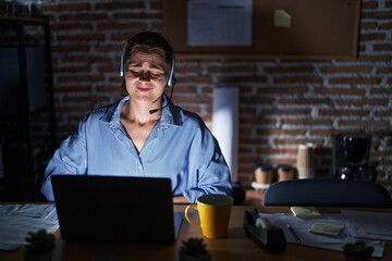 Beautiful brunette woman working at the office at night with hand on stomach because nausea, painful disease feeling unwell. ache concept.