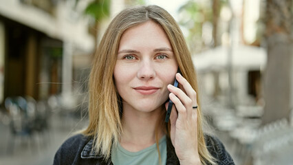 Young blonde woman talking on smartphone with serious expression at street