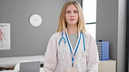 Young blonde woman doctor standing with serious expression at clinic