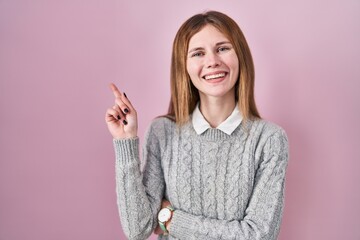 Beautiful woman standing over pink background with a big smile on face, pointing with hand finger to the side looking at the camera.