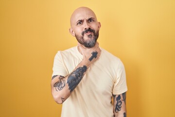 Hispanic man with tattoos standing over yellow background cutting throat with hand as knife, threaten aggression with furious violence