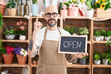 Hispanic man with tattoos working at florist holding open sign surprised with an idea or question pointing finger with happy face, number one