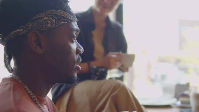 Close up selective focus shot of young African American guy gesturing while telling story to company of friends in cafe