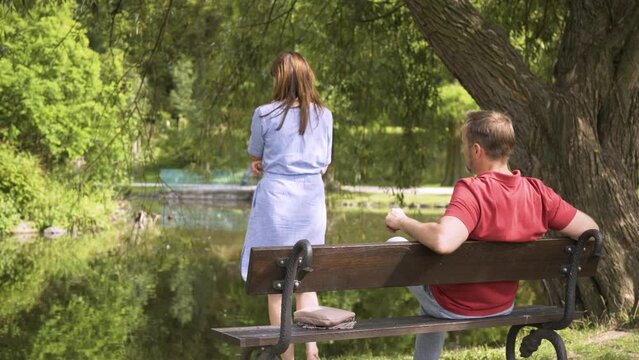 A middle-age couple on a bench in a park - the woman stands up and walks away in thoughts