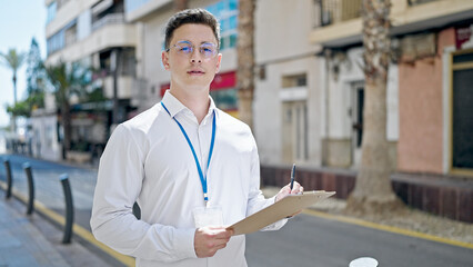 Young hispanic man having survey interview writing on clipboard at street