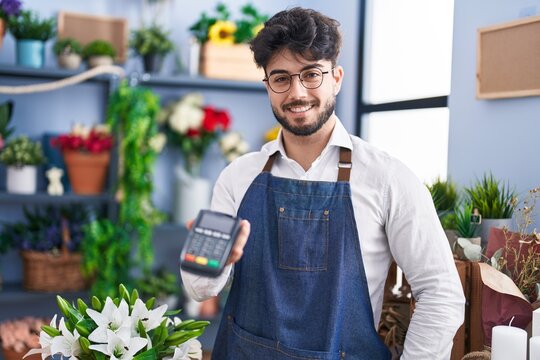 Young hispanic man florist smiling confident holding dataphone at florist shop