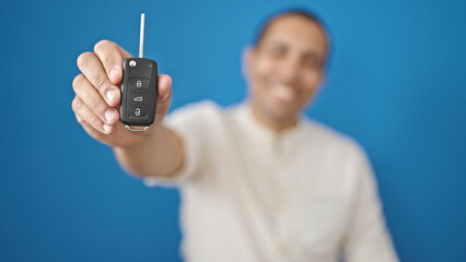 Young hispanic man holding key of new car over isolated blue background