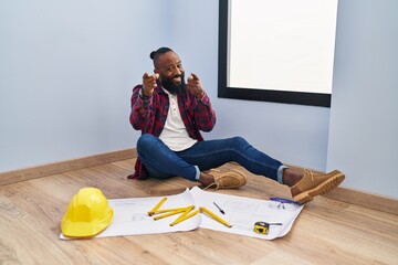African american man sitting on the floor at new home looking at blueprints pointing fingers to...