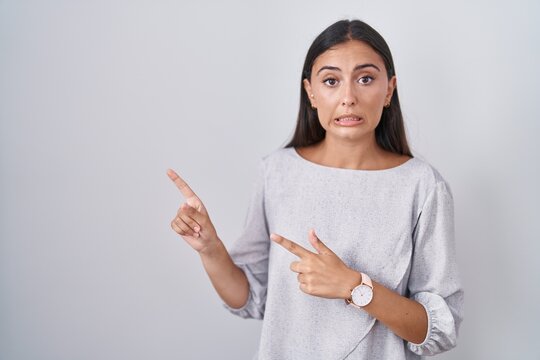 Young hispanic woman standing over white background pointing aside worried and nervous with both hands, concerned and surprised expression
