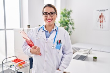 Young beautiful hispanic woman doctor holding medical report standing at clinic