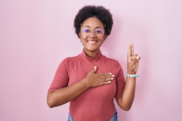 Beautiful african woman with curly hair standing over pink background smiling swearing with hand on...