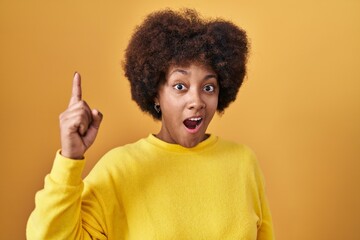 Young african american woman standing over yellow background pointing finger up with successful idea. exited and happy. number one.
