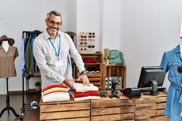 Middle age grey-haired man shop assistant folding clothes at clothing store