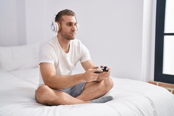 Young caucasian man sitting on the bed at home playing video games relaxed with serious expression on face. simple and natural looking at the camera.