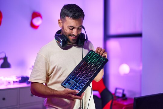 Young hispanic man streamer smiling confident holding keyboard computer at gaming room