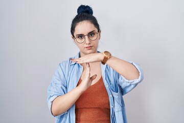 Young modern girl with blue hair standing over white background doing time out gesture with hands,...