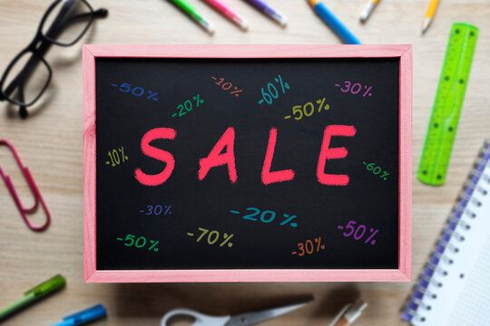 Sale text on chalkboard. Message in chalk on the blackboard on blurred stationery background. Top view on flat lay. Back to School Sales. Template for advertising, website, School supplies store
