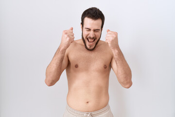 Fototapeta premium Young hispanic man standing shirtless over white background excited for success with arms raised and eyes closed celebrating victory smiling. winner concept.