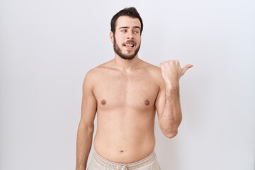 Fototapeta premium Young hispanic man standing shirtless over white background smiling with happy face looking and pointing to the side with thumb up.