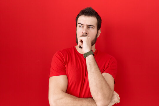 Young hispanic man wearing casual red t shirt thinking worried about a question, concerned and nervous with hand on chin