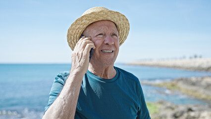 Senior grey-haired man tourist wearing summer hat talking on smartphone at seaside