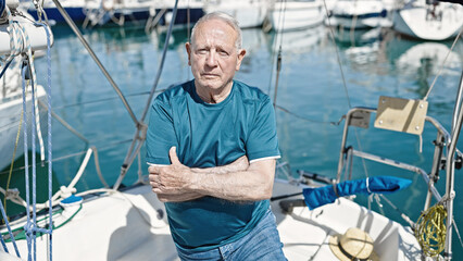 Senior grey-haired man standing with relaxed expression and arms crossed gesture at boat