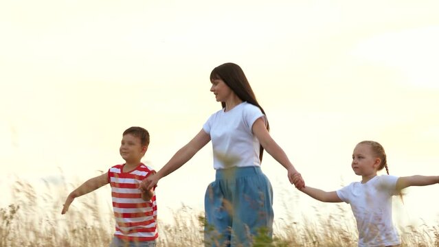 Happy mother with sibling children runs playing plane in field grass at sunset time