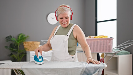 Middle age grey-haired woman listening to music ironing clothes at laundry room