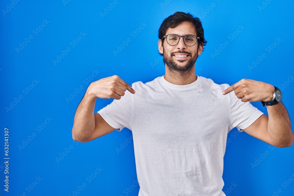 Sticker handsome latin man standing over blue background looking confident with smile on face, pointing ones