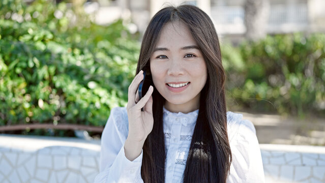 Young chinese woman speaking on the phone sitting on bench at park