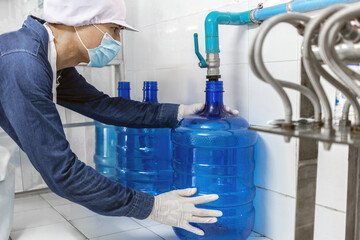 A worker in workwear and with a protective mask on his face produces drinking water in a clean factory. clean drinking water production line
