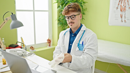 Fototapeta premium Young hispanic man doctor using laptop wearing gloves at the clinic