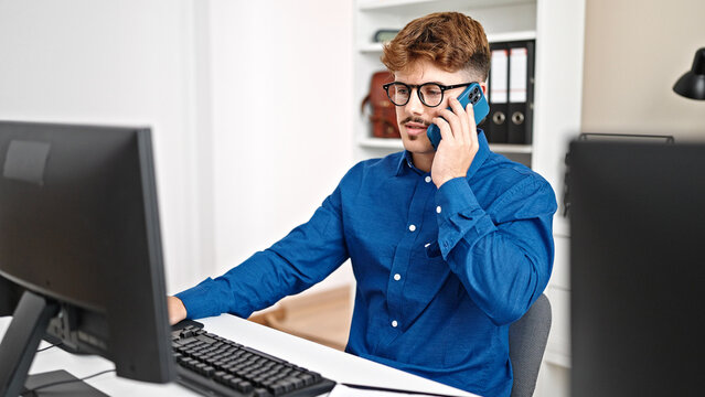 Young hispanic man business worker using computer talking on smartphone at the office