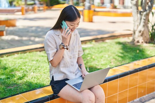 Chinese woman using laptop talking on smartphone at park