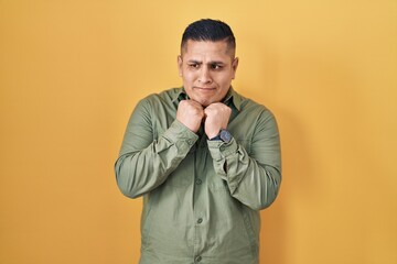 Fototapeta premium Hispanic young man standing over yellow background laughing nervous and excited with hands on chin looking to the side