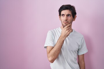 Young hispanic man standing over pink background thinking worried about a question, concerned and nervous with hand on chin