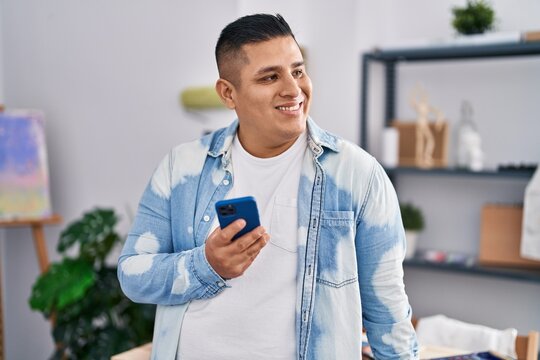 Young latin man artist smiling confident using smartphone at art studio