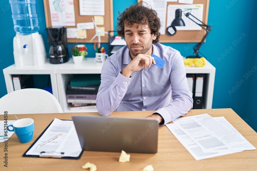 Canvas Prints Young hispanic man business worker using laptop and credit card with doubt expression at office