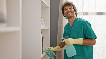 Young hispanic man cleaning shelving with a cloth smiling at home