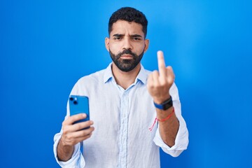 Hispanic man with beard using smartphone typing message showing middle finger, impolite and rude...