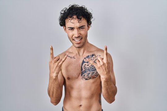 Hispanic man standing shirtless shouting with crazy expression doing rock symbol with hands up. music star. heavy concept.