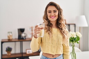 Young woman drinking glass of water standing at home