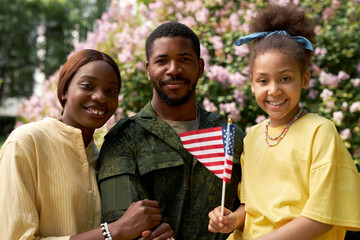Portrait of African American family of three with american flag smiling at camera while standing...