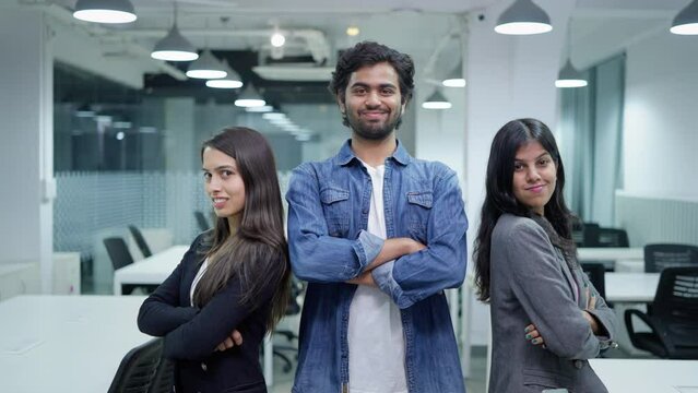 Three young happy Asian Indian intern male and female office employees standing with crossed arms looking at the camera and smiling in a modern start up corporate business workplace