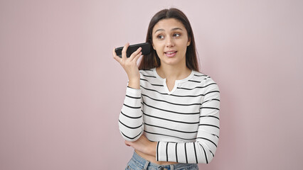 Young beautiful hispanic woman listening to audio message by the smartphone over isolated pink background