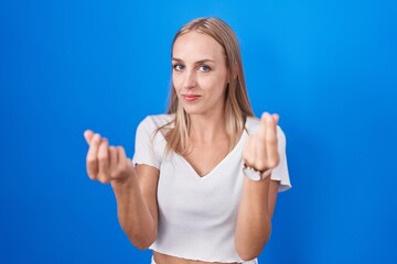 Young caucasian woman standing over blue background doing money gesture with hands, asking for salary payment, millionaire business