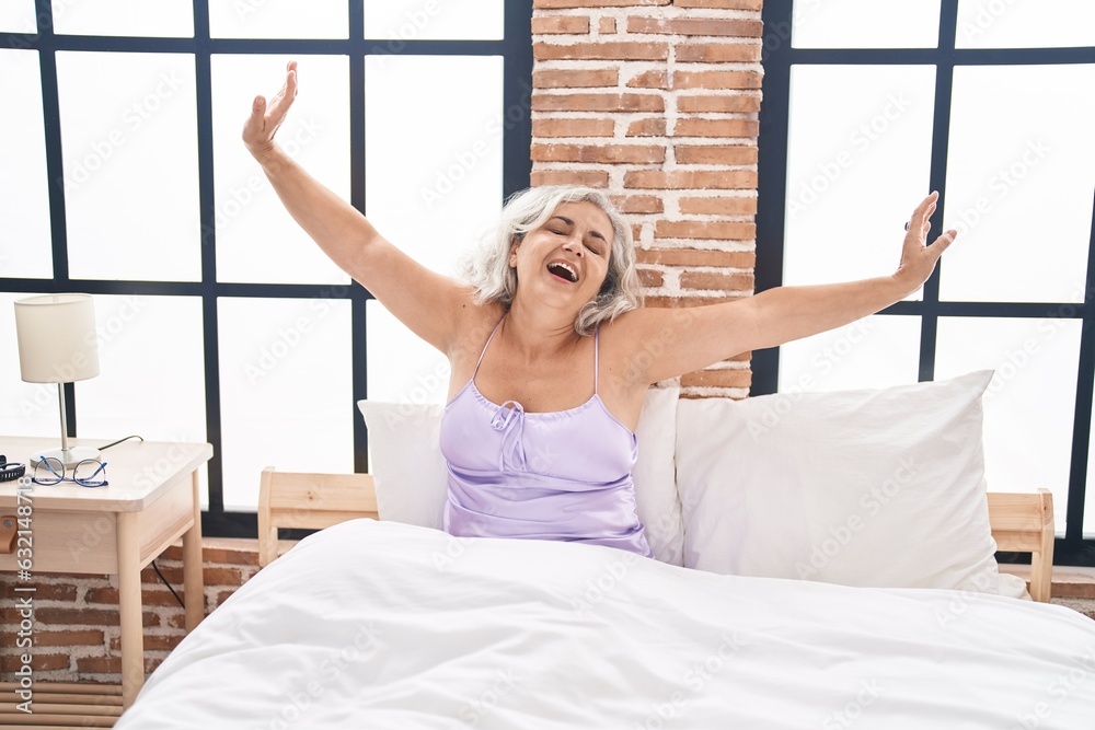 Poster middle age grey-haired woman waking up stretching arms at bedroom