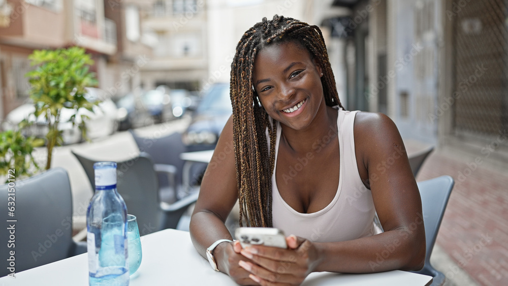 Canvas Prints African american woman using smartphone sitting on table smiling at coffee shop terrace