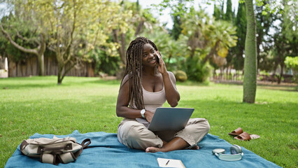 African american woman student using laptop talking on smartphone at campus university