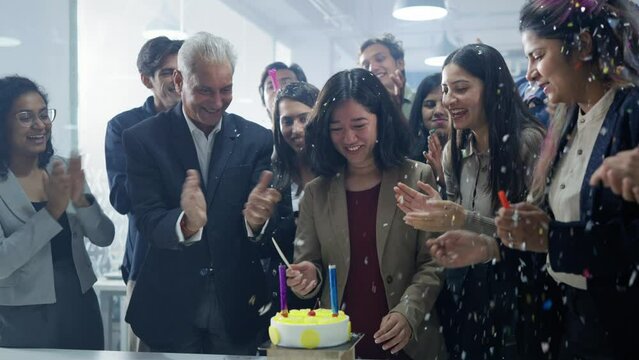 A happy, excited group or team of corporate employees smiling and celebrating together a birthday of a young female office colleague or intern girl by surprising with cake in modern start up business.
